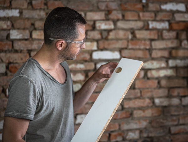 The carpenter looks at the hole in the wood.